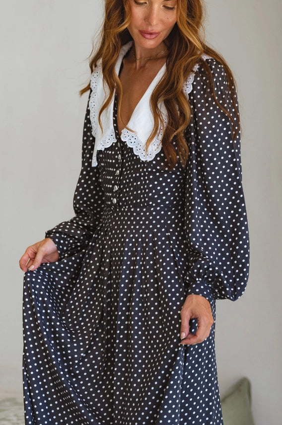 Model holding flowing skirt of black polka dot midi dress with lace collar