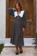 Model wearing a black polka dot midi dress with a white lace-trimmed collar and long sleeves
