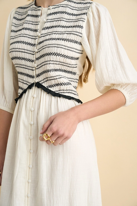 Close-up of black smocking, covered buttons and crochet trim on ecru organic cotton dress